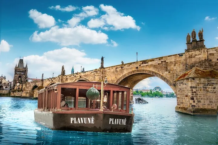 Una piccola barca da canale di legno chiamata Plavuně che passa sotto un arco di pietra di Ponte Carlo in una giornata soleggiata